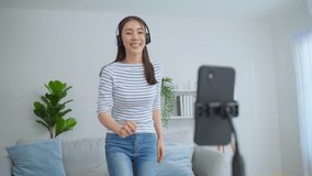 Asian attractive woman enjoy dance with music in living room at home. Beautiful female use mobile phone recording challenge video virtual clip sing a song, enjoy weekend activity lifestyles in house.
