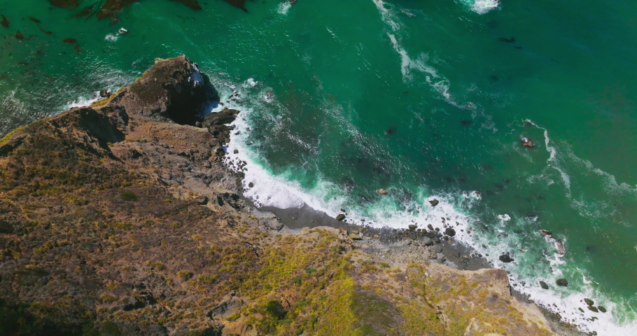 Beautiful aquamarine sparkling in the sun water of Pacific ocean in California, USA. Rocky rugged shore meeting the foamy waves. Bird