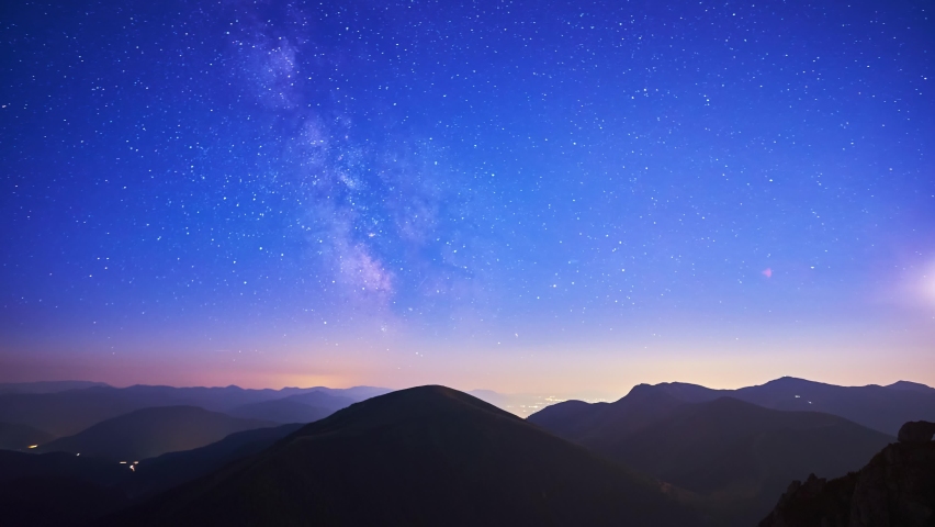 The stars of the Milky Way galaxy move above the mountain hills. From night to day. 4K Royalty-Free Stock Footage #1094313875