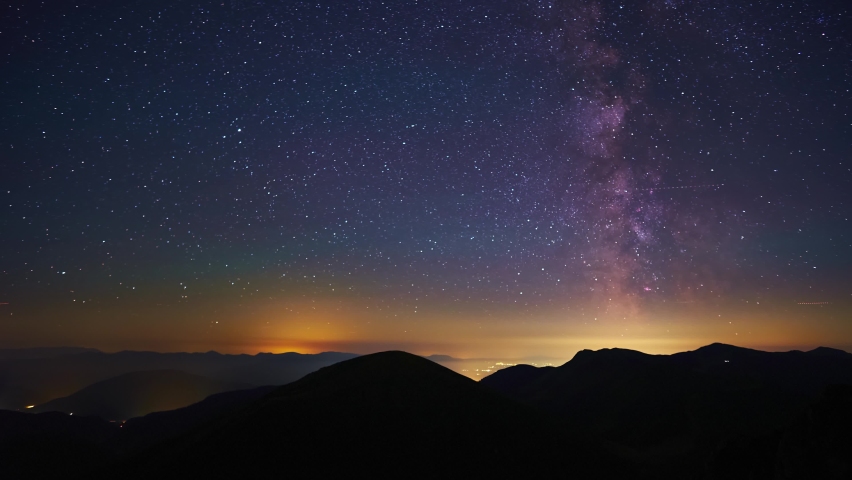 The stars of the Milky Way galaxy move above the mountain hills. From night to day. 4K
