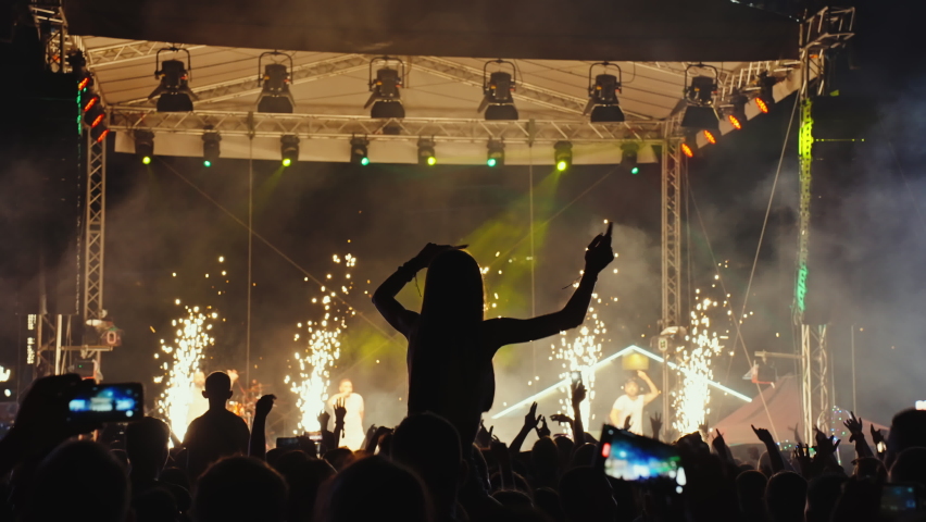 Music concert Silhouettes of fans at a music show, concert. Festival of youth music. Laser stage show. Crowd of fans raised their hands, applause.  Symbol made of fingers. Lifestyle. 