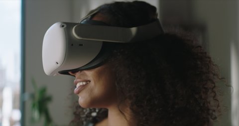 DOLLY IN Attractive African American female puts on a VR virtual reality metaverse headset at home Vídeo Stock