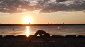 Slow motion video of a woman doing yoga workout on Baltic sea coastline during sunset