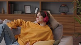 Enjoy listening to music. Young woman relaxing on sofa with eyes closed wearing red headphones. Portrait of woman in earphones at home. Relaxation, leisure and stress management. - Powered by Shutterstock - Get 15% off with code: PIKWIZARD15