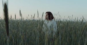 A beautiful young woman of European appearance, dressed in a white sweater, walks through the field among the ears of wheat, touching them with her hands. Video from the evening, 4k. 3D Illustration