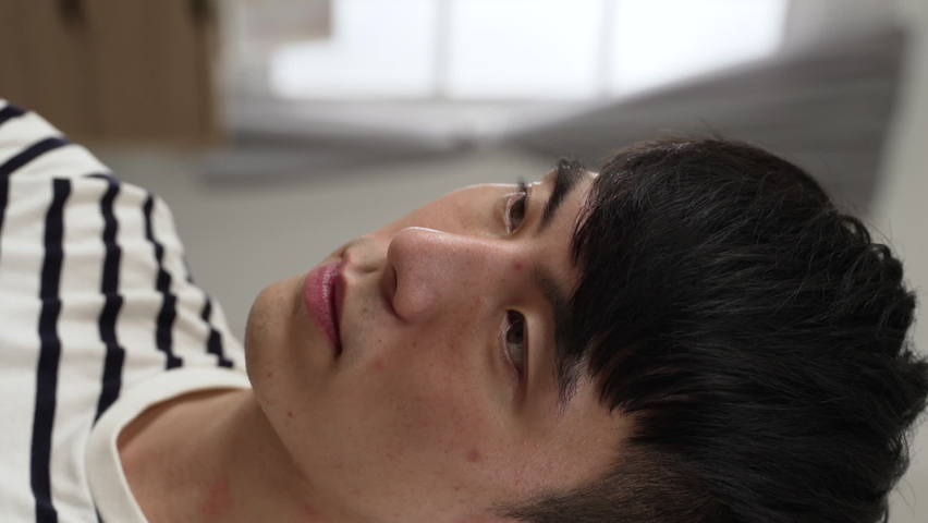 Vertical Screen: headshot of a smiling asian Korean man drinking tea from cup and looking away into distance with a sigh of relief while working from home at daytime.
