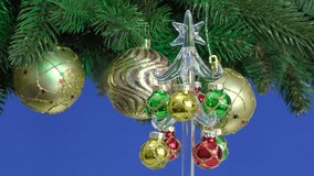 On a blue background, a small Christmas tree rotates near a rotating large Christmas tree decorated with Christmas balls