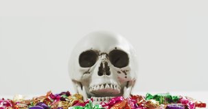 Animation of halloween text over skull with sweets on grey background. Halloween, autumn, fall, festivity tradition and celebration concept digitally generated video.