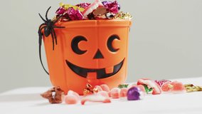 Animation of halloween text over carved pumpkin bucket with sweets on grey background. Halloween, autumn, fall, festivity tradition and celebration concept digitally generated video.