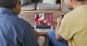 Video of diverse male friends sitting on sofa and watching football on laptop at home. Sports, competition and spending family time at home.