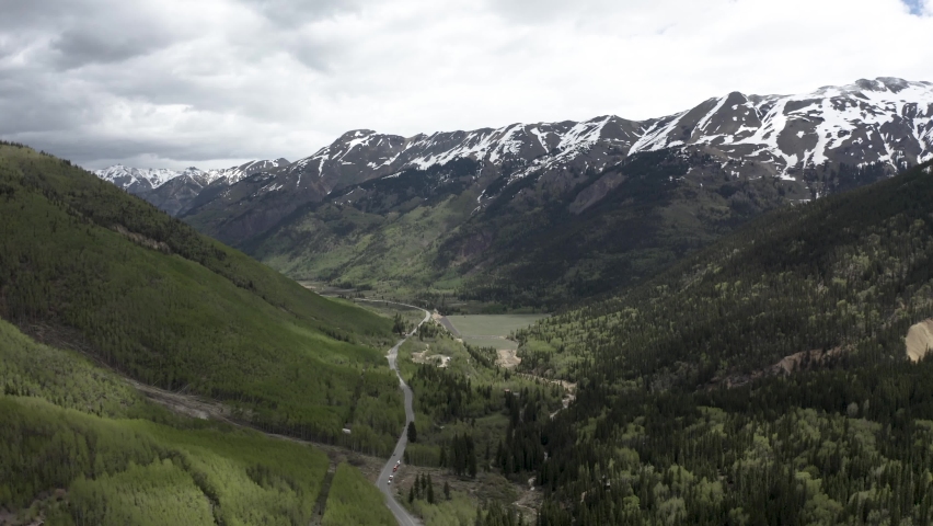 Colorado Rocky Mountains with snowed peaks and small lake below, Aerial flyover shot