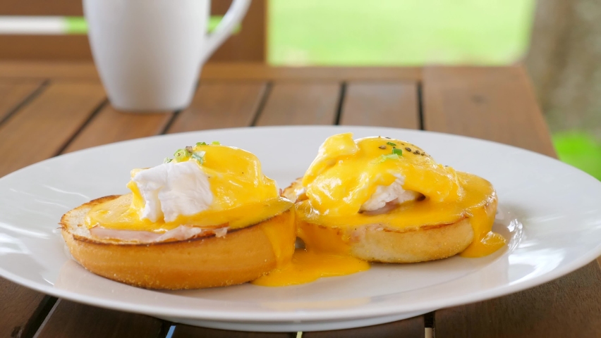 Healthy breakfast food. Toasts with poached eggs on plate in restaurant. Woman eating delicious Eggs Benedict with hollandaise sauce. Female hands cuts egg with liquid egg yolk inside. Close up. Royalty-Free Stock Footage #1094347391