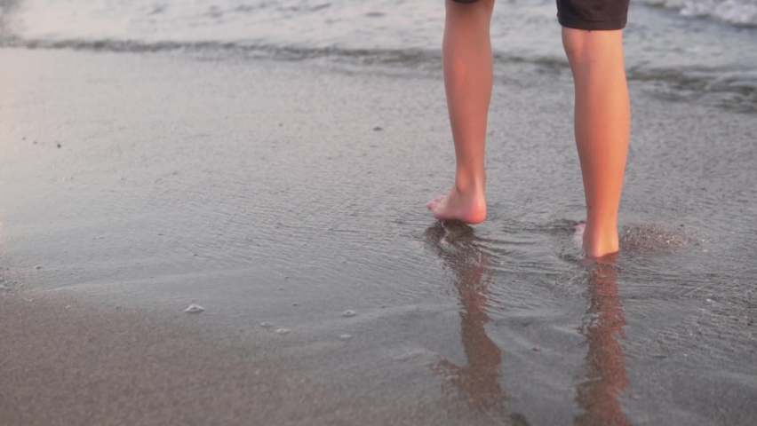 Close-up of the feet of a teenager walking along the beach by the sea.