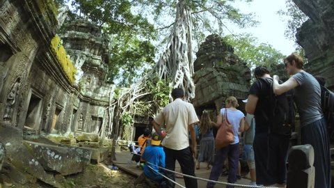 SIEM REAP, CAMBODIA - NOVEMBER 03, 2014: Streams of tourists take turns posing in time-lapse in front of the Ta Prohm temple in the Angkor complex, which suffers from overcrowding.