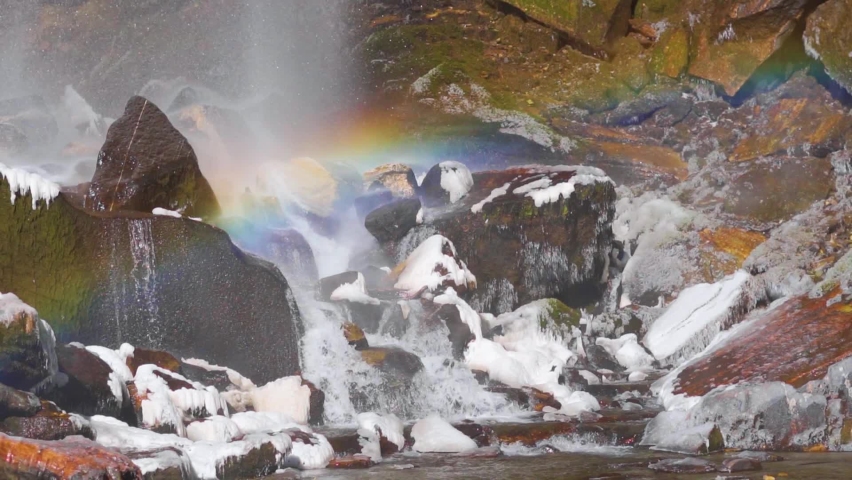 Handheld slow motion shot of rainbow formed under the Jogini waterfall on top of snow covered rocks during the winter season at Manali in Himachal Pradesh, India. Rainbow forms under the waterfall. | Shutterstock HD Video #1094351801