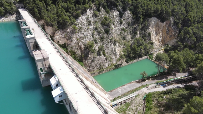 Amazing water dam with people walking, lush green forest and sunny warm weather.