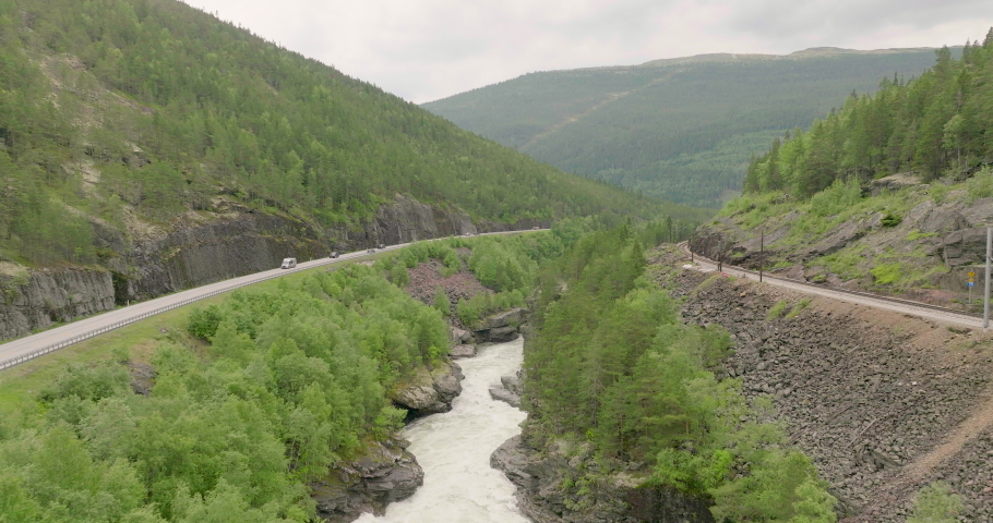 Thaw water running through rocky valley with cars on road and train track