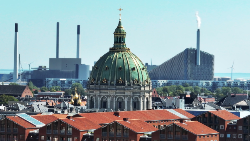Beautiful large dome of Frederiks Kirke against zoomed background. Power plant and wind farm on seashore. Copenhagen, Denmark