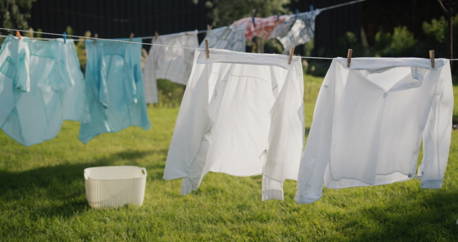 Clothes and bedding are drying in the backyard of the house, a laundry basket is standing on the grass nearby. | Shutterstock HD Video #1094365811