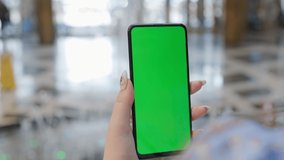 Back view of brunette holding chroma key green screen smartphone watching content. Hand holds mobile phone and scrolls up web page . Gadgets and contemporary people concept. Use online payment