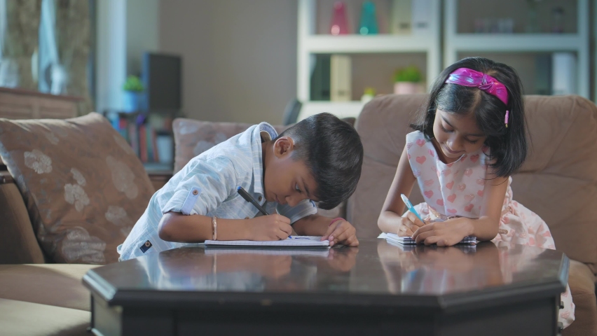 A modern Indian Asian adorable girl and a boy or a sister and brother busy writing or drawing on a notebook or notepad sitting in an interior home. study, Learning, education, homeschooling concept Royalty-Free Stock Footage #1094366441