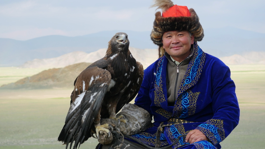 Kazakh Eagle Hunter in traditional clothing holding a golden eagle on his arm near Bayan-Olgii in West Mongolia.