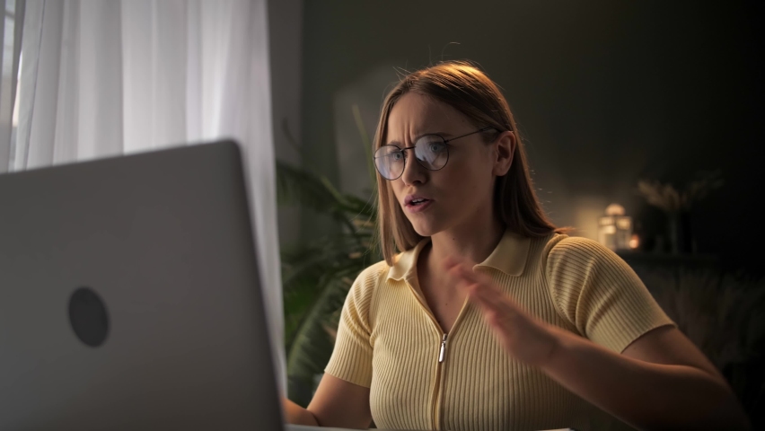 young woman remote works in home office, sitting at table with laptop. has video call using web cam, argues, blows up and disputes. Looks angry and dissatisfied. girl swears using online network. High Royalty-Free Stock Footage #1094370061