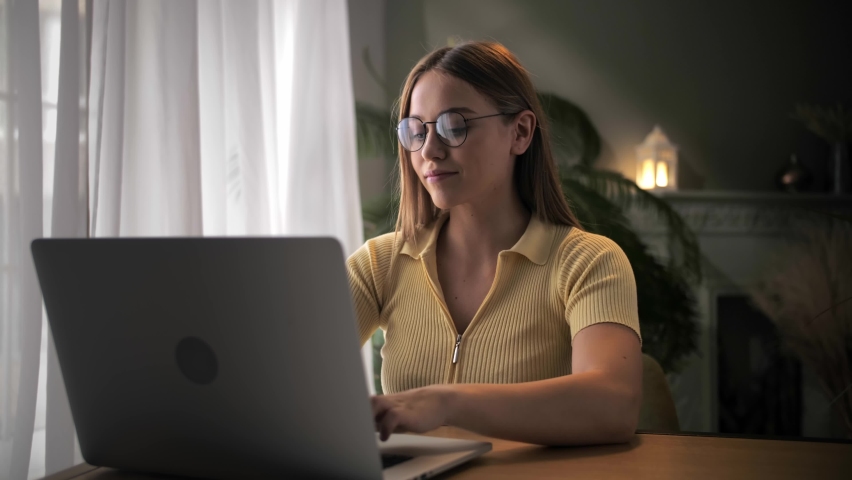 Woman work remotely using laptop sitting at table in home interior.Young blonde hair girl typing on keyboard computer and learning online class indoors.Serious female doing work with notebook. High Royalty-Free Stock Footage #1094370085