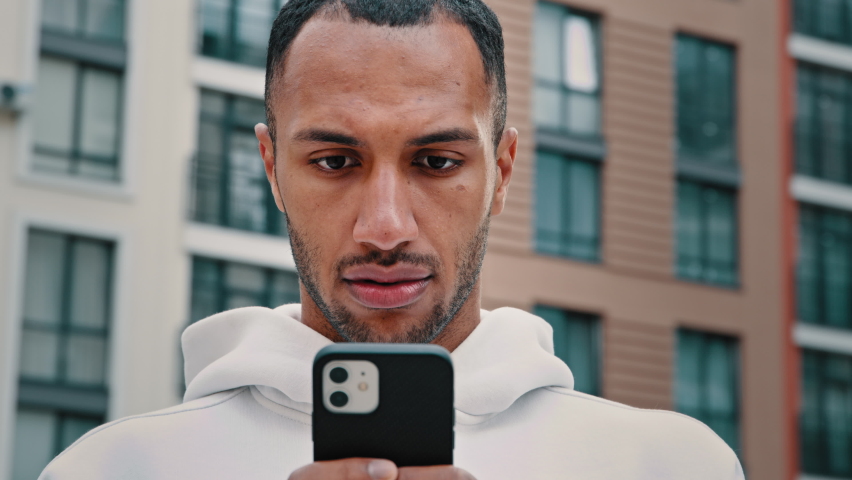 Upset male face biracial latino sad lost guy stands on city street holds mobile gadget, looks at smartphone reads unpleasant bad message confused facial emotion looks around waits for meeting outdoors Royalty-Free Stock Footage #1094372003