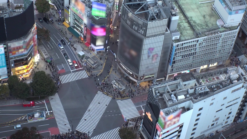 SHIBUYA, TOKYO, JAPAN : Wide aerial high angle view of SHIBUYA CROSSING in sunset. Crowded downtown area. Japanese city life, people and urban metropolis concept. Long time lapse shot, dusk to night. Royalty-Free Stock Footage #1094373519