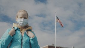 A child in a protective mask stands against the background of a school and a US flag. - Powered by Shutterstock - Get 15% off with code: PIKWIZARD15