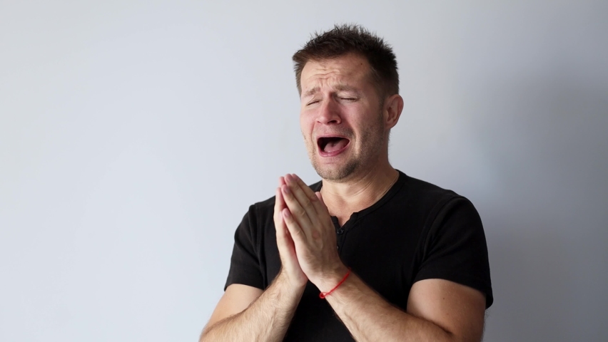 Handsome man in black t-shirt scratches his nose and sneezes loudly | Shutterstock HD Video #1094381173