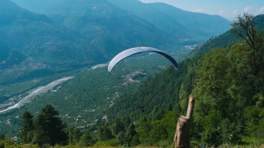 Tourist paragliding on parachute in background of green mountain valley and river during summer at Dobhi ,Manali in Himachal Pradesh. Adventure sports activity in India.  | Shutterstock HD Video #1094381185