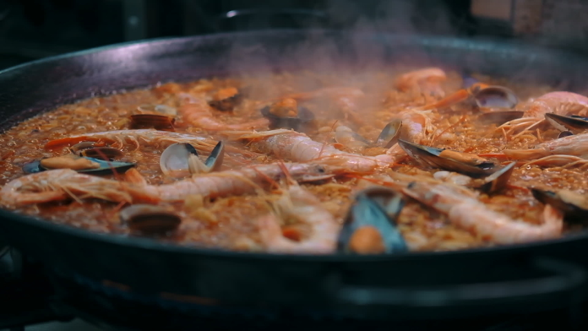 Close up slow motion view seafood paella cooked on frying pan. Traditional Spanish dish. Restaurant main course dish concept
