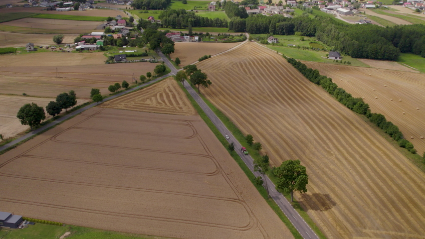 Tracktor with carrier transporting hay bales on a countryside road in Poland with the harvested field around - aerial tracking field 
