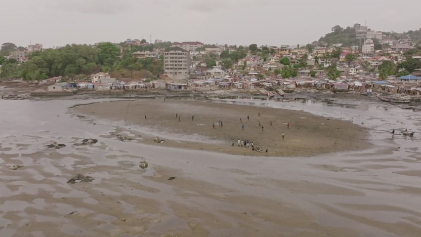 Rotating aerial footage of a group of men playing soccer on a sandbank in Freetown, Sierra Leone.