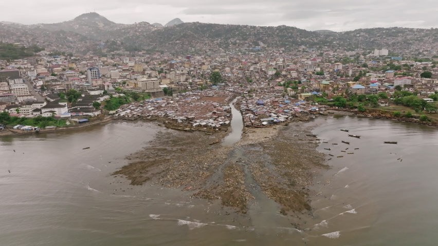 Aerial footage of a creek emptying out into the bay outside of Freetown, Sierra Leone with trash flowing out.