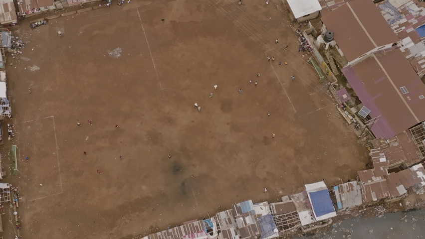 Slow aerial footage that is zooming out of people walking around an empty soccer field in Freetown, Sierra Leone.