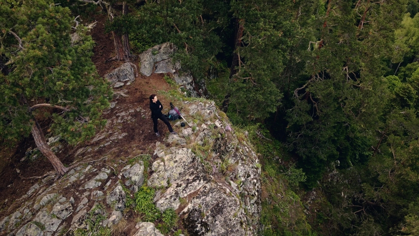 Aerial pedestal tilt shot of female adventure hiker reaching top of wild viewpoint