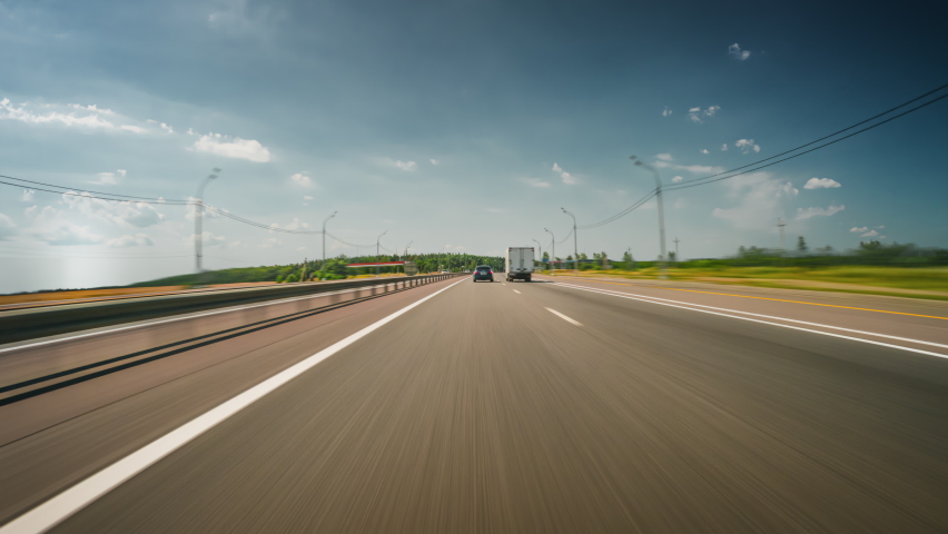Beautiful motion timelapse of a fast road drive along the highway on a sunny summer day. Front view from the car window to the road and surrounding landscapes. Royalty-Free Stock Footage #1094392845