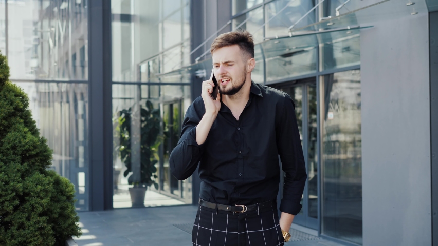 Stressed young business man hearing awful news at mobile phone call conversation. Unhappy entrepreneur worker looking angry, listening complaints from client talking on smartphone wave hands stress. | Shutterstock HD Video #1094394029