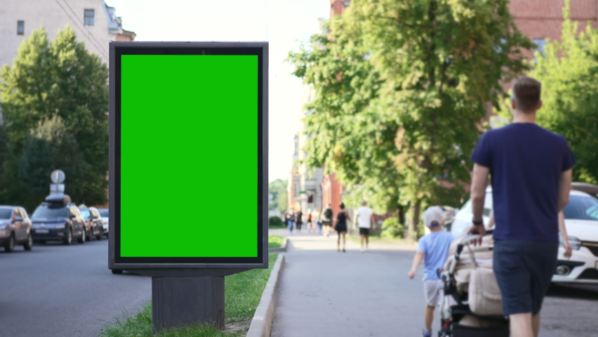4k Mockup billboard stands and people walk in city street spbd. Green empty poster is standing and pedestrians walking in modern town on summer day. There is vertical screen designed for advertising Royalty-Free Stock Footage #1094394227
