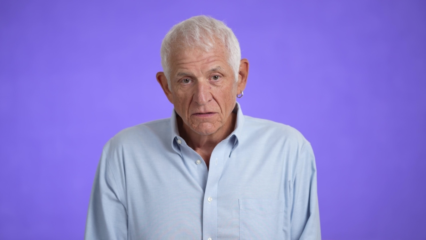 Sad upset worried disturb displeased shocked elderly gray-haired man 70s talking wears blue shirt sigh surprise put hands on face isolated on solid purple background studio portrait | Shutterstock HD Video #1094397375