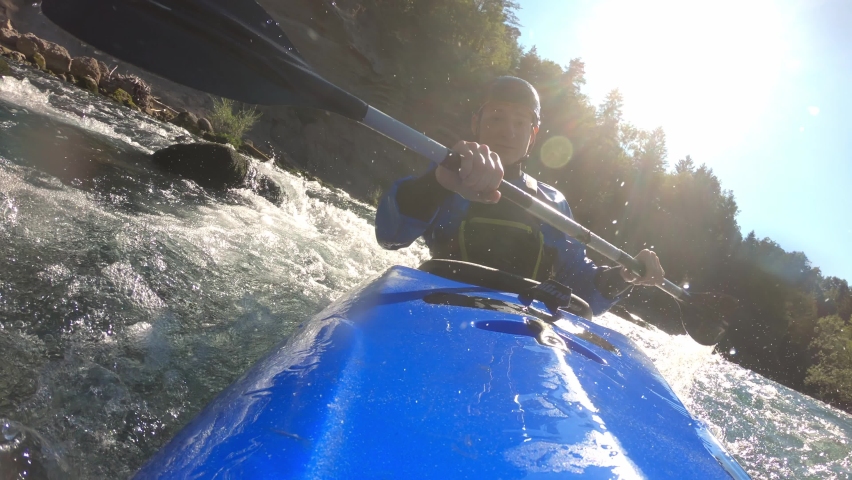 Male athlete enjoying kayaking over fast moving mountain river, skillfully paddling and maneuvering, front view.