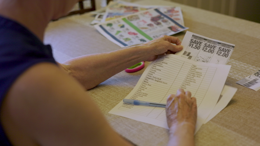 A senior woman clipping coupons from a newspaper flyer to help with the inflated cost of living. Royalty-Free Stock Footage #1094398889