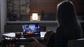 Aspiring female musician greeting her distant guitar teacher on online video call on laptop indoor. Woman improving guitar playing skills while watching online master class. High quality 4K footage
