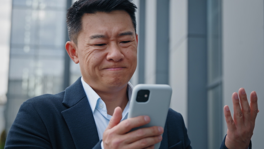 Close up Asian middle-aged adult man mad unhappy businessman feeling annoyed with using broken smart phone low battery problem angry having problem with mobile telephone frustrated bad news outdoors | Shutterstock HD Video #1094413963