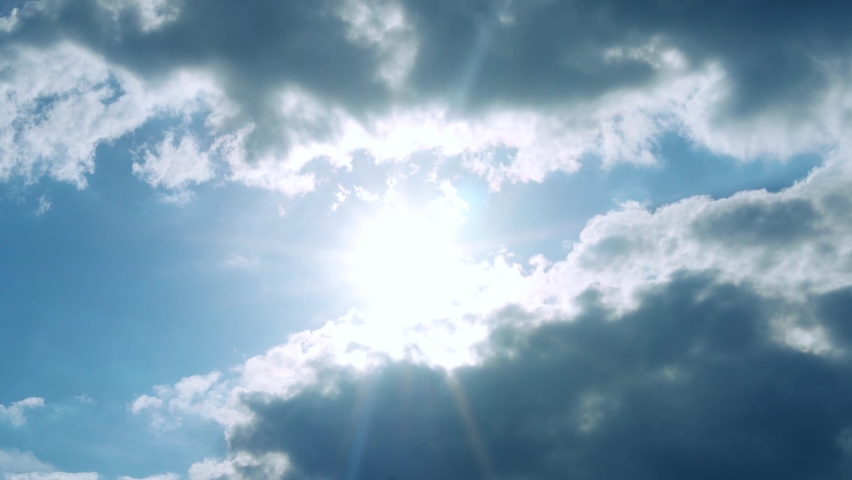 Beautiful Blue Sky Glowing Sun Between Two Puffy Cumulus Dark Clouds, Slow Motion, Time Lapse. Sunshine Sunlight Beams and Glare, Beauty, Relax, Backgrouds. Bright Sunny Day, Sunny Sky in Sunbeams.
