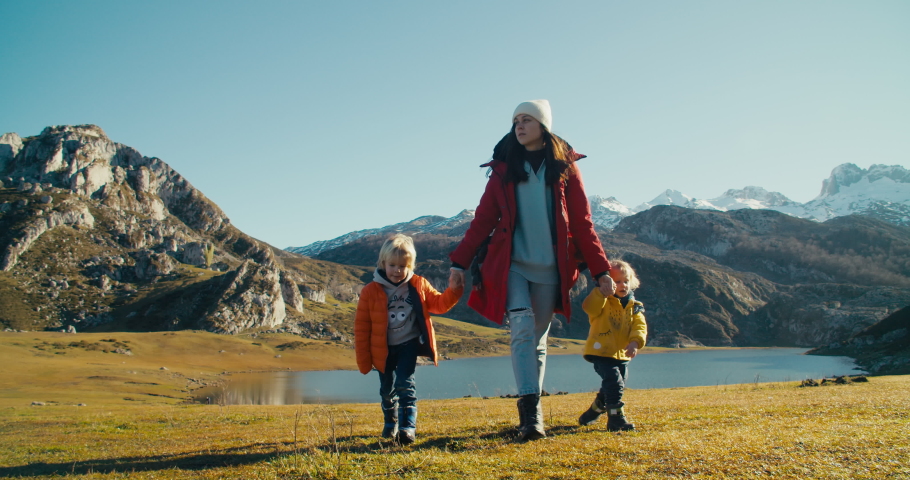 Woman hold children hand and walk on tourist path at mountain lakeshore on epic nature landscape. Family on vacation travel adventure enjoy together of freedom. Mother with kids leads active lifestyle Royalty-Free Stock Footage #1094415357