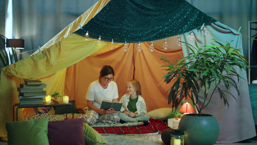 A very wholesome moment of a child spending his time with his mother and laughing away as she reads out to him a story from a book they re both sitting down in a snug